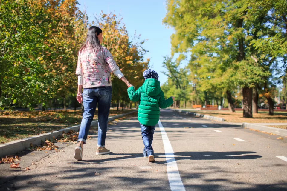Parent and child walking, holding hands on mixed-use trail with trees